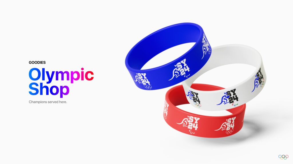 Gros plan sur trois bracelets en silicone (bleu, blanc et rouge) disposés en cercle sur un fond blanc. Chaque bracelet arbore le logo SYD24 avec le kangourou stylisé. À gauche, le texte « Boutique Olympique » apparaît dans un dégradé de couleurs vives, accompagné du slogan « Les champions sont servis ici »